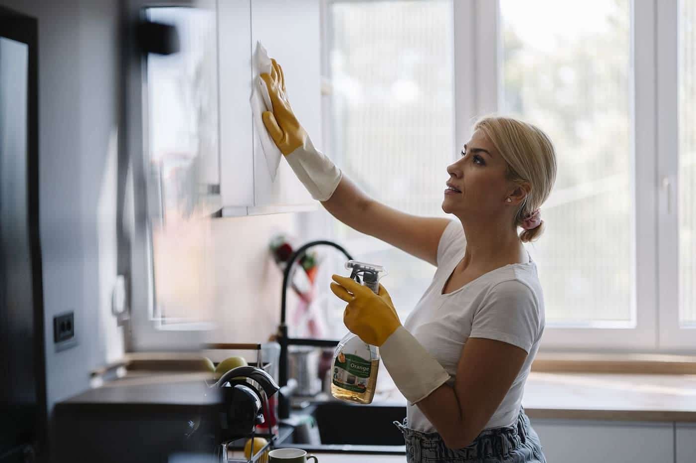 A woman cleaning kitchen cabinets in a bright kitchen