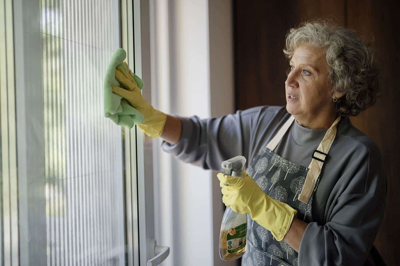 A woman cleaning a window with a cloth and spray cleaner